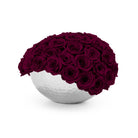 White spherical vase filled with deep purple roses on a white background