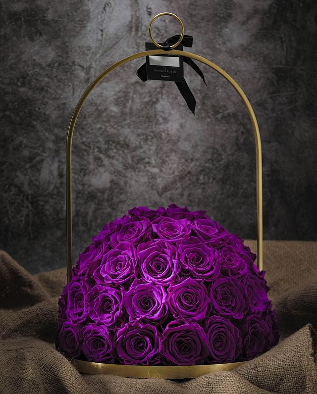 Purple roses in a gold metal dome on a textured surface with a dark background